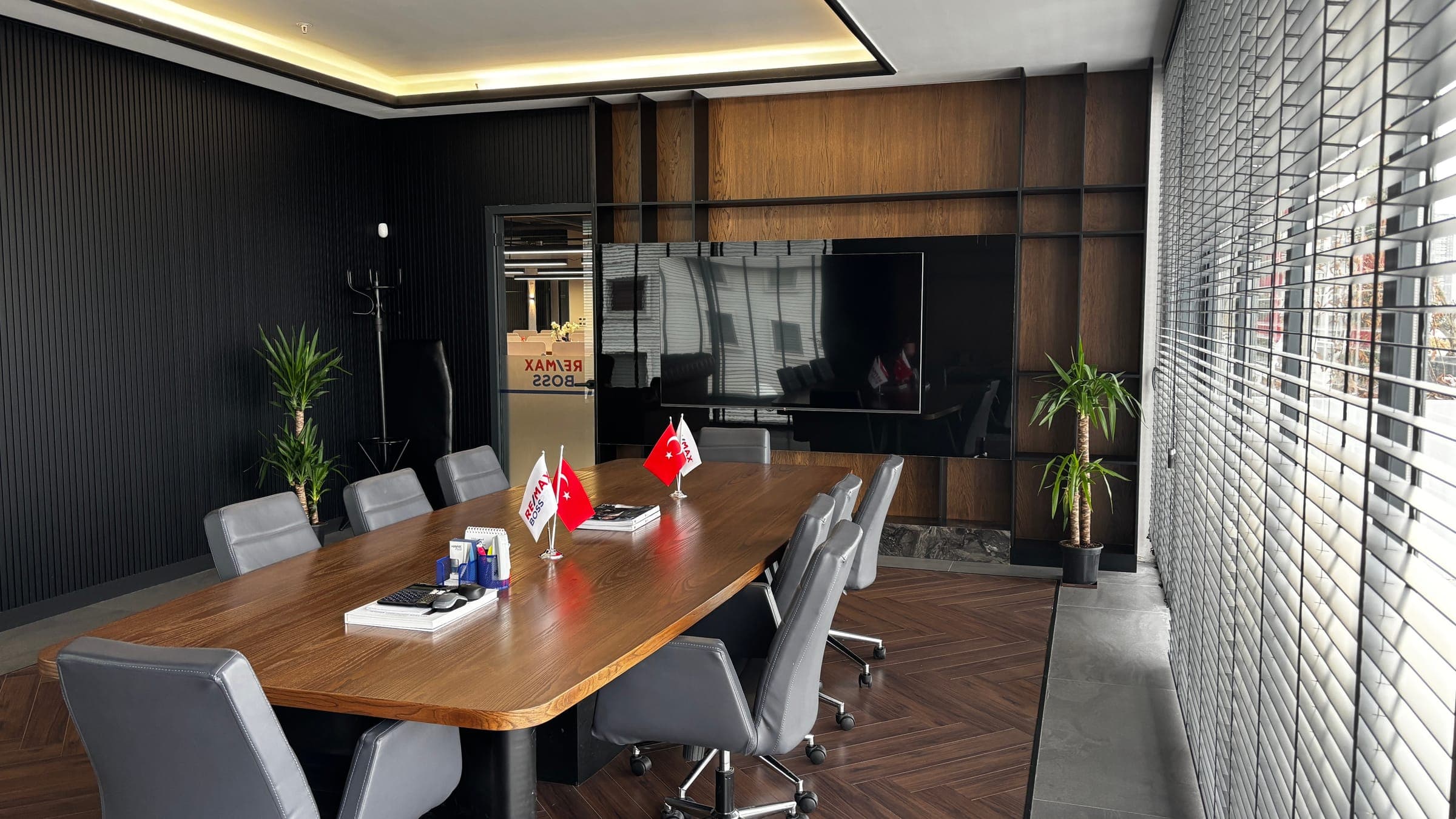 RE/MAX BOSS toplantı odası — ahşap masa, Türk bayrağı ve RE/MAX BOSS bayrakları